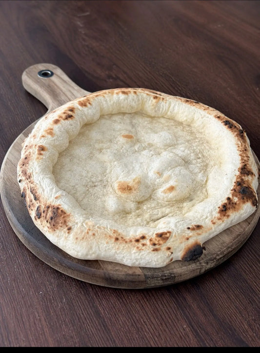 A baked Neapolitan pizza base on a wooden paddle board, The image highlights 48-hour fermentation, Italian Tipo 00 flour, and handmade in Dorset production details.