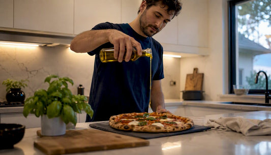 Man drizzling olive oil on pizza in kitchen