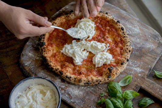Hands adding stracciatella cheese to hot pizza
